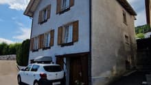 2-story house with gray exterior walls, brown wooden shutters, and a parked car in the driveway.