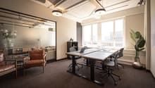Empty office room with desks and chairs, large windows, potted plant, leather chair, small table