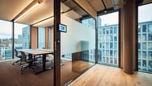 An empty conference room with glass walls, a table, chairs, and a monitor on the wall.