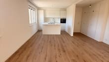 large open space, kitchen island with sink and faucet, wooden floors, white walls, ceiling lamps, storage cabinets, window with white frame