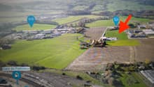 Aerial view of a rural area with fields, buildings, and a railway. The highlighted area shows a small house with a red arrow pointing towards it.