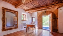 Dining room: Wooden floor, wooden dining table and chairs, ornate mirror, wooden ceiling with chandelier, wooden door, window with white shutter