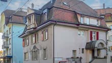 Two-story house, gray exterior, red roof, multiple windows, balcony on the second floor, chimney