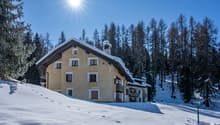 2-story house, beige exterior, covered in snow, balconies, pine trees in the background