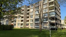 Multi-story apartment building with balconies, surrounded by trees and grass.