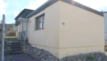 Single-story house, beige exterior, single window, metal railing, steps leading to entrance, gravel pathway