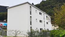 white building, several windows, fenced area, mountain in the background