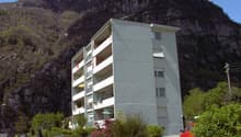white apartment building, several balconies, mountain landscape, red cars parked