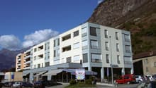 apartment building with balconies, several stories, cars parked in front