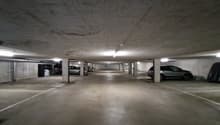 concrete floor, white ceiling, rows of parking spots, lights on the ceiling, metal columns, some cars parked