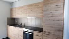 Modern and minimalistic kitchen with wooden cabinets, black countertops, built-in oven and sink with faucet, light fixtures
