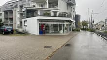 An apartment building with several floors and a storefront at the ground floor, with a car parked in front of it.
