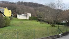 A sloping garden with trees and bushes, fenced on one side, and overlooking the hills.