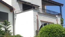 White stuccoed house, covered balcony with metal railings, chimney, metal guttering, glass window
