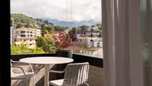 outdoor balcony with table and chairs, glass railing, potted plant, city view, mountain view