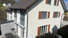 2 story house, white exterior, brown roof, brown shutters, large windows, patio with table and chairs
