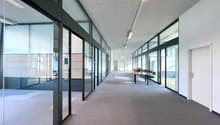 Empty office hallway with glass walls, carpeted floor, meeting room table and chairs, fluorescent lights