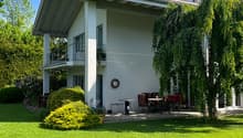 modern house with 2 floors, red tiled roof, large balcony on 2nd floor, garden with lawn and trees, outdoor dining area