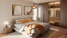 Modern styled bedroom with wooden floor, a large double bed with white bedding, two paintings on the wall, nightstand with a lamp and a small plant, and a built-in wardrobe with glass doors.