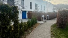 White house with a brick pathway, garden, and hedges in front of it.