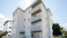 Modern white building, multiple balconies, multiple floors, fenced area in front