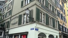 A multi-story building with green shutters, a pharmacy sign on the side, and a fire hydrant in front.