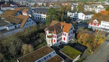 Two story house with brown roof, red windows, balcony, small garden