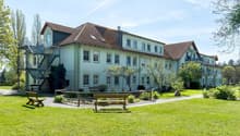 2 story house, white walls, brown roof, multiple windows, stairs, balcony, garden, benches