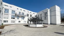 Modern white building, multiple windows, balconies, brick driveway, gazebo, car parked