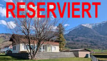 Detached house, brown roof, white walls, glass windows, surrounded by a grassy field, mountains in the background
