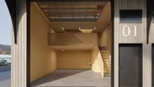 Exterior view of a building with a raised ground floor, wooden walls, and a staircase leading to the upper floor.