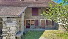 Stone house, brown roof, wooden doors, wooden shutters, wooden bench, stone wall, grassy area