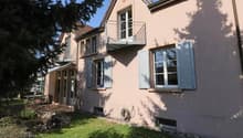 Two story house, pink walls, white shutters, balcony, large tree, garden, patio with table, ground-level access to basement
