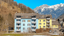 multi-story residential building, balconies on each floor, snow on ground, mountainous background
