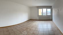 empty room with white walls, tiled floor, large window, heating radiator