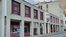 Two-story building, brick construction, red shutters, signage for various shops, multiple entrances