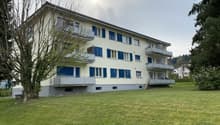 3 story apartment building, white walls, blue shutters, balconies, large grassy area