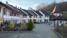 Row of houses, white walls, black roofs, red shutters, brick driveway, small garden in front, trees in the background