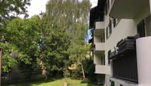 Building with balconies, grassy lawn, several trees, wooden bench, metal railings