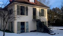 white exterior, brown roof, chimney, stairs leading to front door, snow-covered ground, two-story, multiple windows