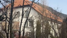 White house, red tiled roof, several windows, surrounded by trees, located on a hill