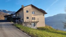 detached 3 story house with raised ground floor, green landscape, driveway, lake and mountain view