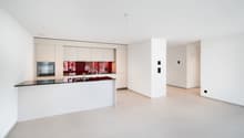Modern, open-concept kitchen with white cabinets, black countertops, and a red glass backsplash. The kitchen is integrated into the living space and has a clean, minimalist design.