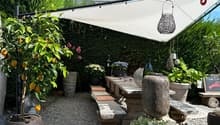 Outdoor dining area with a large table, stone benches, umbrella, plants, and decorative elements