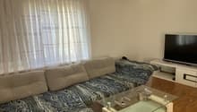 L-shaped sofa, glass coffee table, flat screen TV, white curtains, wooden floor