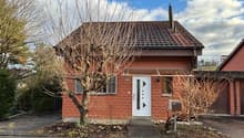 red brick small house, white door, windows with white shutters, chimney