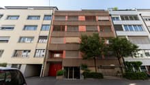 Modern multistory apartment building with multiple balconies, garage entrance, trees, and bicycle racks