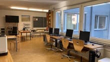 room with several wooden desks, chairs, monitors, shelves, and blackboard