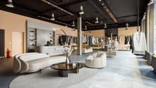Large open space with concrete floors, black ceiling with track lighting, display racks and shelves for clothing, a curved white sofa and coffee table in the center, and a reception desk at the back of the store.