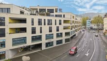 Modern multistory building, white walls, multiple garages, windows, balconies, visible mountain range